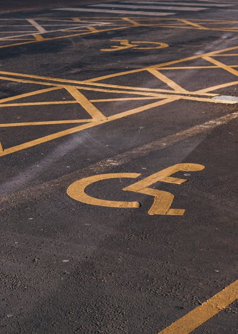 A blue parking sign indicating a designated parking space for individuals with disabilities, mounted on a metal pole in front of a dark grey wall. The sign features a large white 'P' and a wheelchair