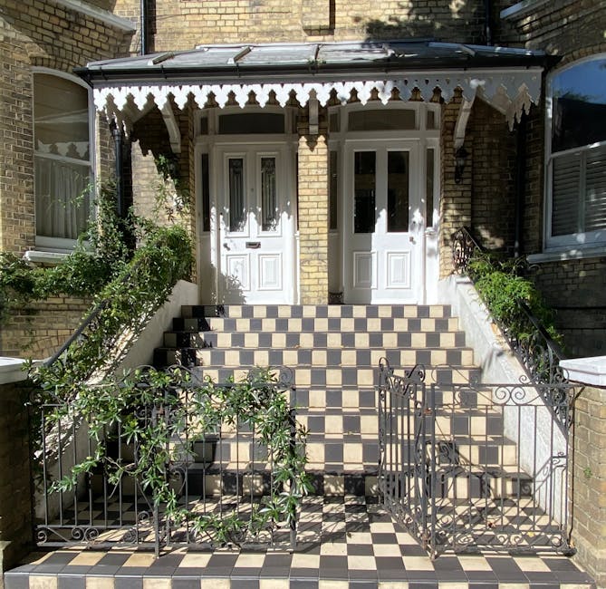 A row of traditional Victorian-style terraced houses constructed from light brown brick, with white-framed sash windows and small decorative balconies. The houses are positioned directly adjacent to a